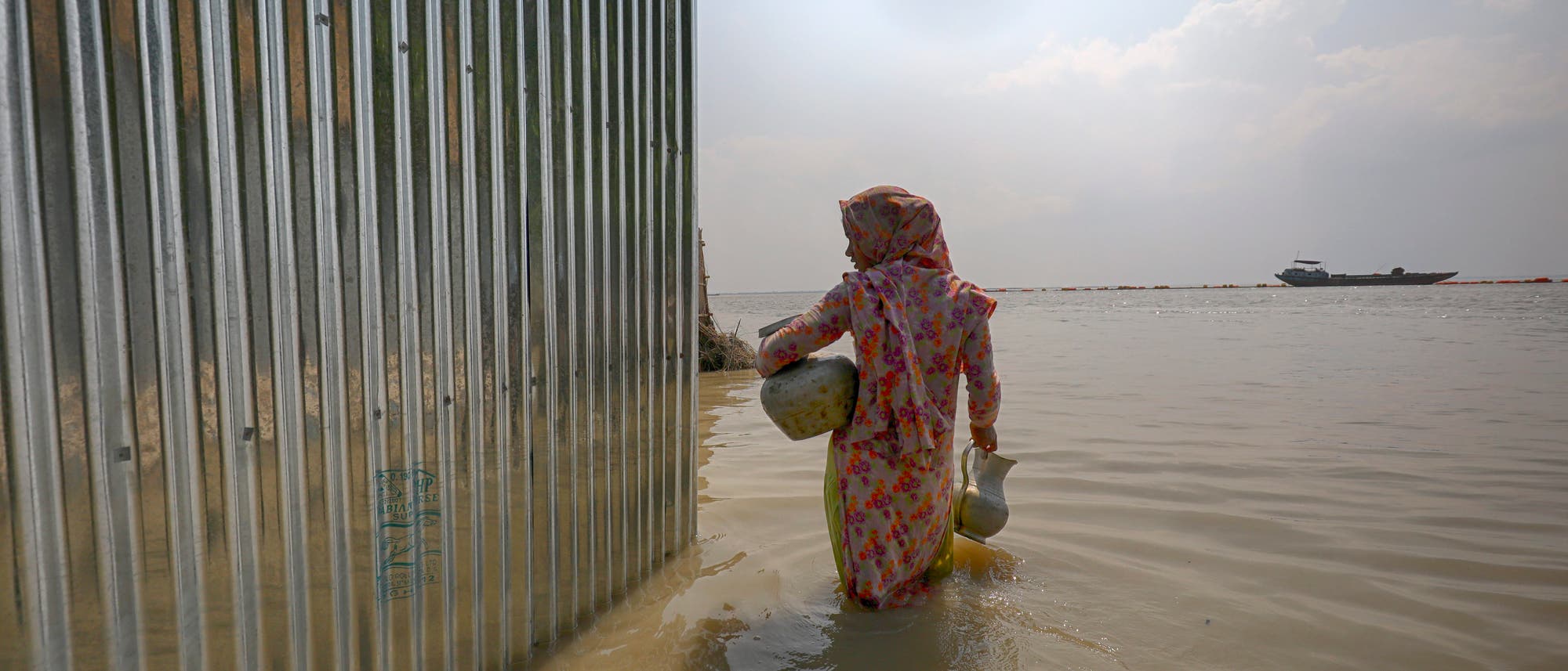 Eine Frau mit Trinkwasserbehältern watet im Juli 2019 durch kniehohes Wasser im überfluteten Jamalpur-Distrikt Eine Frau mit Trinkwasserbehältern watet im Juli 2019 durch kniehohes Wasser im überfluteten Jamalpur-Distrikt