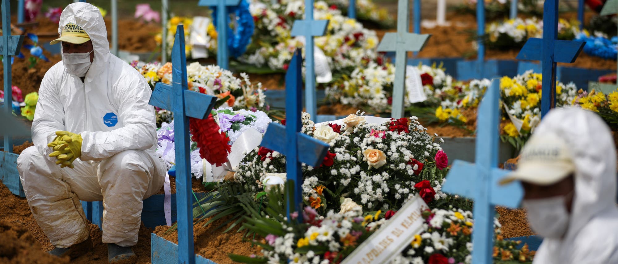 Friedhofsmitarbeiter in Schutzanzügen sitzen auf mit Blumen geschmückten Gräbern während einer Beerdigung am Friedhof Nossa Senhora Aparecida in Manaus. Friedhofsmitarbeiter in Schutzanzügen sitzen auf mit Blumen geschmückten Gräbern während einer Beerdigung am Friedhof Nossa Senhora Aparecida in Manaus.