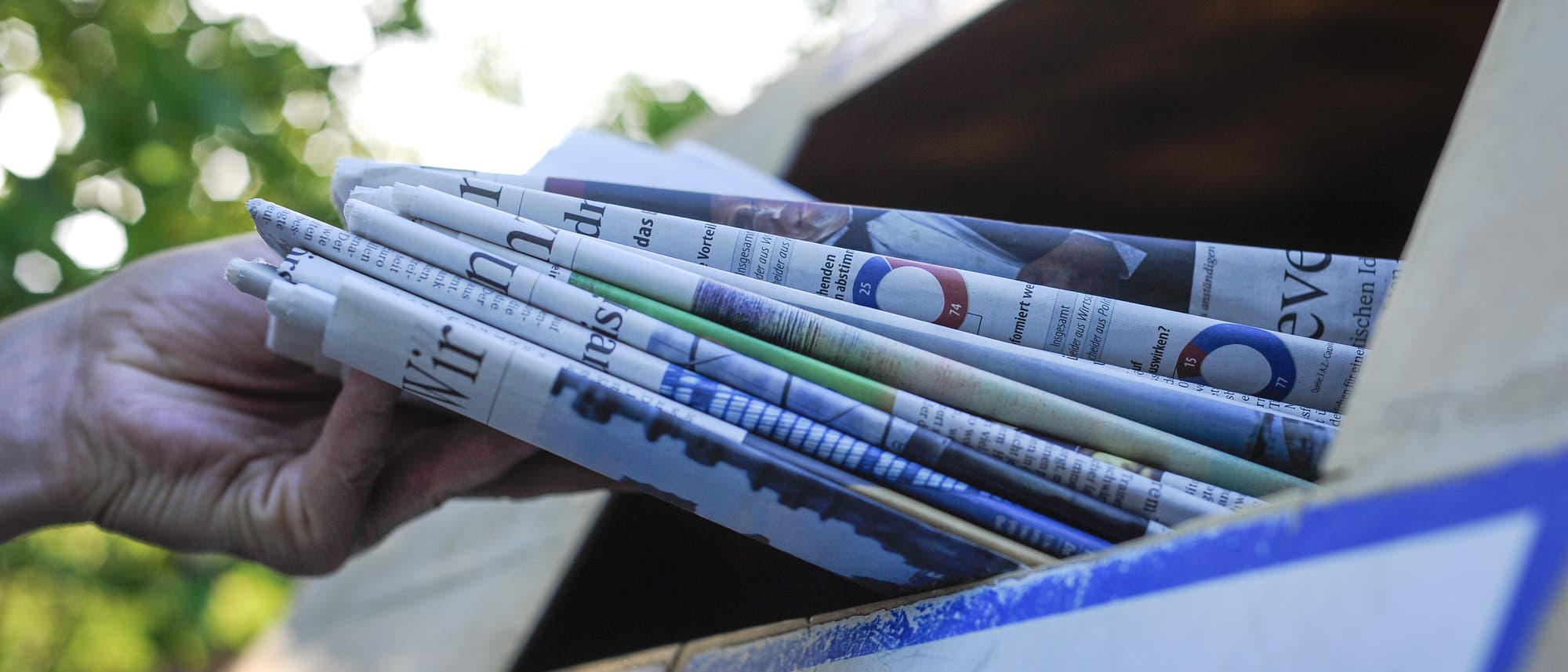 Eine Hand schiebt einen Stapel Zeitungen durch den Schlitz eines Altpapiercontainers. Eine Hand schiebt einen Stapel Zeitungen durch den Schlitz eines Altpapiercontainers.