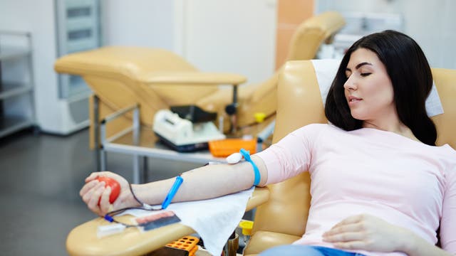 Eine junge Frau sitzt in einem Sessel und spendet Blut in einer Art medizinischem Zentrum.