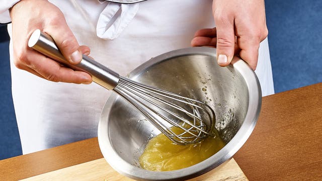 Herstellung von Mayonnaise in einer Edelstahlschüssel mit Handrührer.