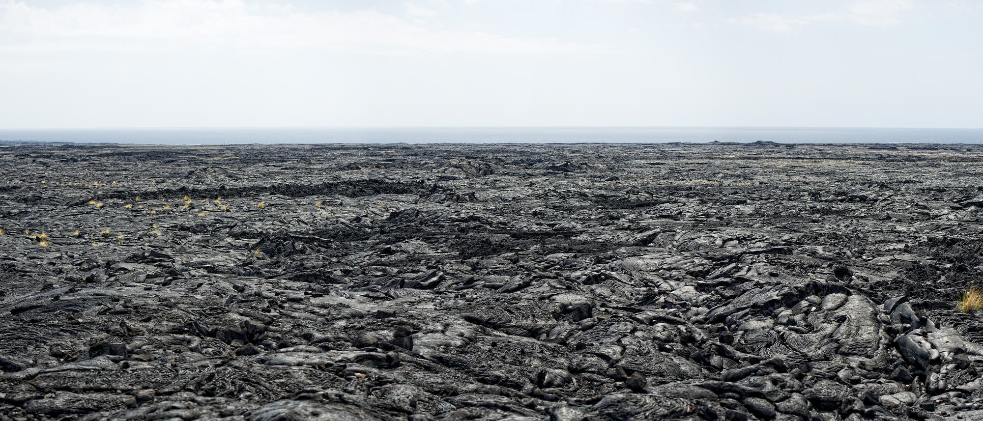 Flaches Lavafeld erstreckt sich zum Horizont, dahinter Meer und dunstiger Himmel Flaches Lavafeld erstreckt sich zum Horizont, dahinter Meer und dunstiger Himmel
