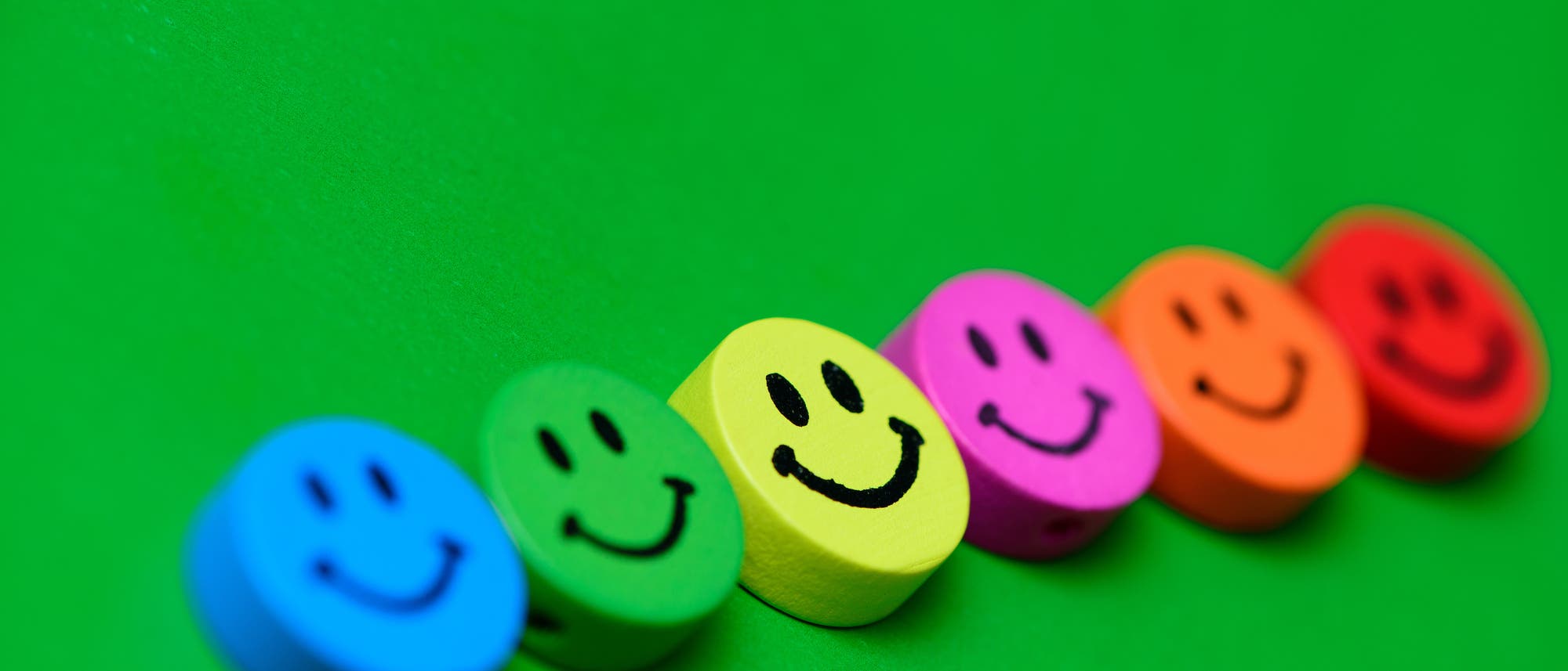 Eine Reihe bunter Smiley-Holzklötze auf grünem Grund Eine Reihe bunter Smiley-Holzklötze auf grünem Grund