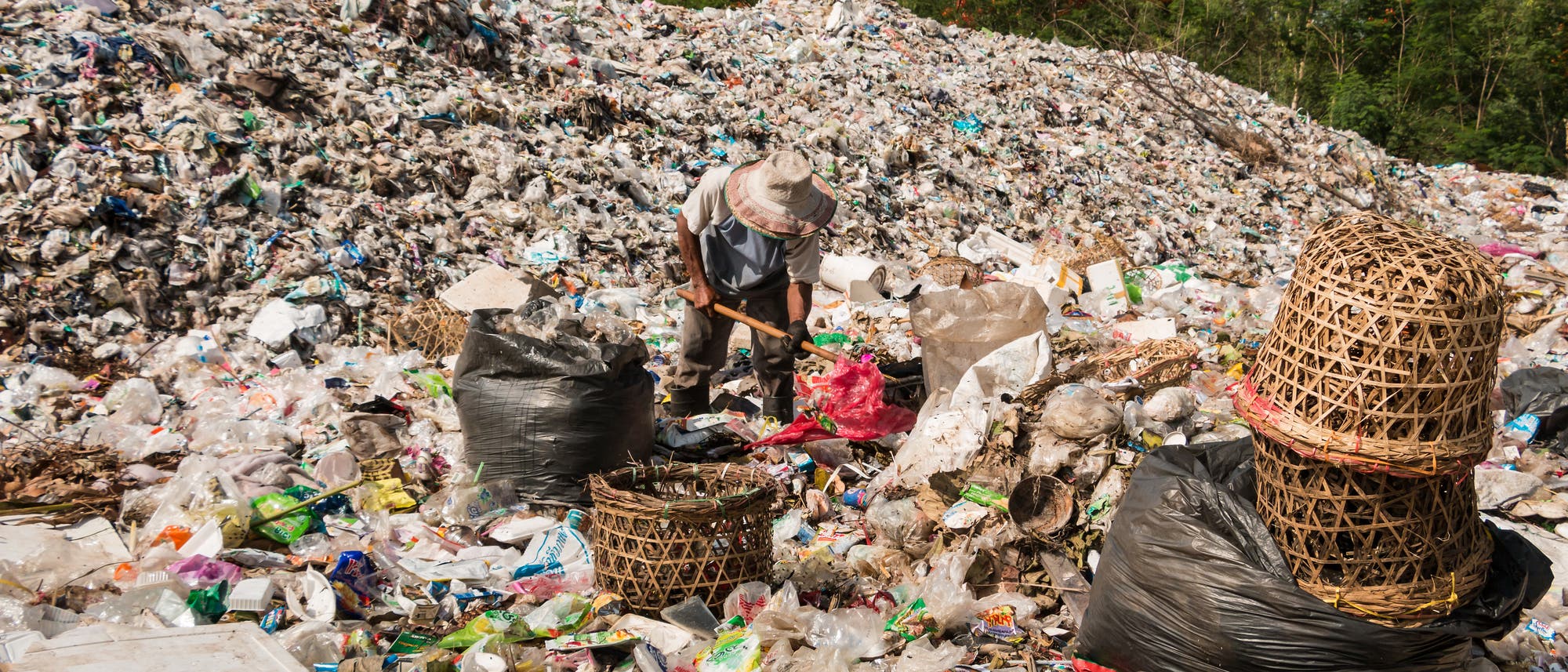 Ein Mann mit Strohhut durchforstet eine Mülldeponie