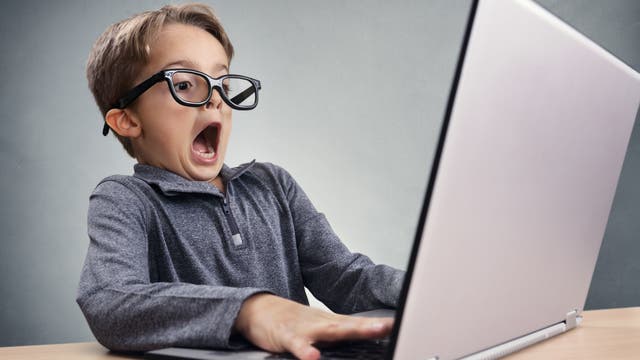 Kind mit Hemd und Brille sitzt vor einem Monitor und guckt übertrieben erschrocken