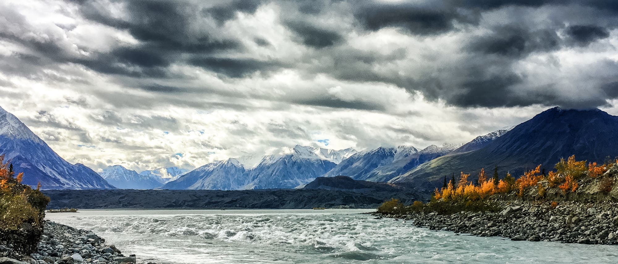 Ein breiter Schmelzwasserfluss zwischen Ufern mit Tundrenbewuchs. Im Hintergrund hohe Berge, darüber dramatische Wolken. Vermutlich haben die Autoren das Bild von der örtlichen Tourismuszentrale. Ein breiter Schmelzwasserfluss zwischen Ufern mit Tundrenbewuchs. Im Hintergrund hohe Berge, darüber dramatische Wolken. Vermutlich haben die Autoren das Bild von der örtlichen Tourismuszentrale.