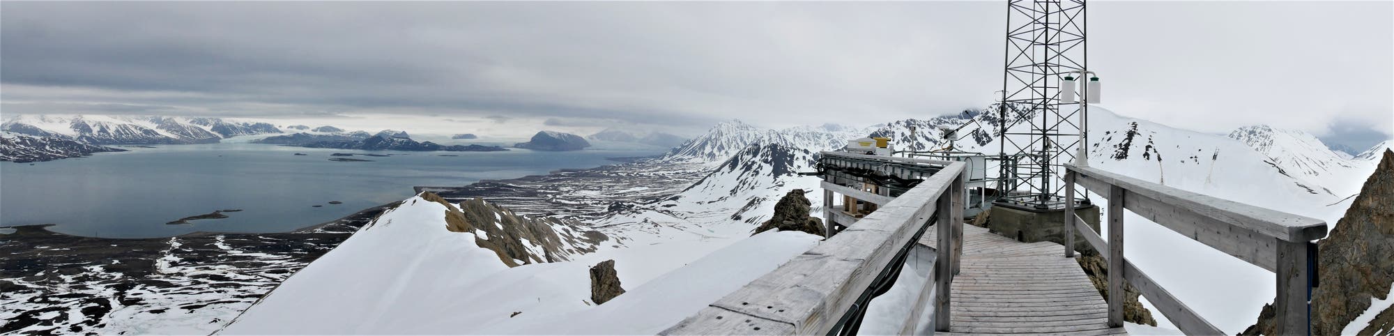 Panoramaaufnahme von der Terrasse des Zeppelin-Bergs über Ny-Ålesund und den Fjord auf Berge und Gletscher am anderen Ufer.
