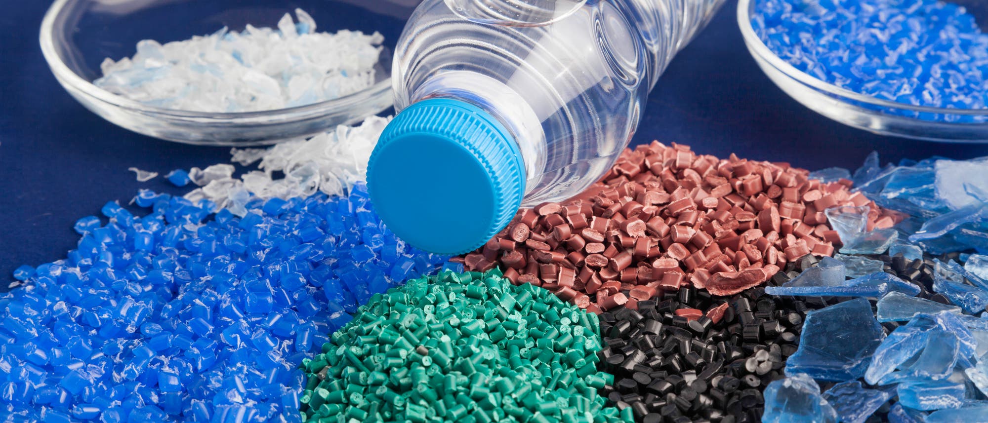 Plastikgranulat in verschiedenen Farben, in der Mitte eine PET-Flasche Plastikgranulat in verschiedenen Farben, in der Mitte eine PET-Flasche