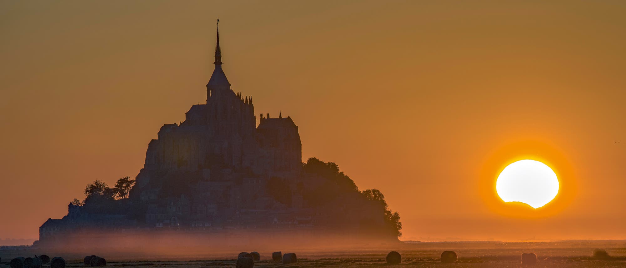 Die Klosterinsel Mont-Saint-Michel in der Normandie, eine Welterbestätte der UNESCO, bildete am 21. August 2017 eine malerische Kulisse für einen besonderen Sonnenuntergang. Teilweise vom Mond bedeckt, sank unser Tagesgestirn unter den Horizont.