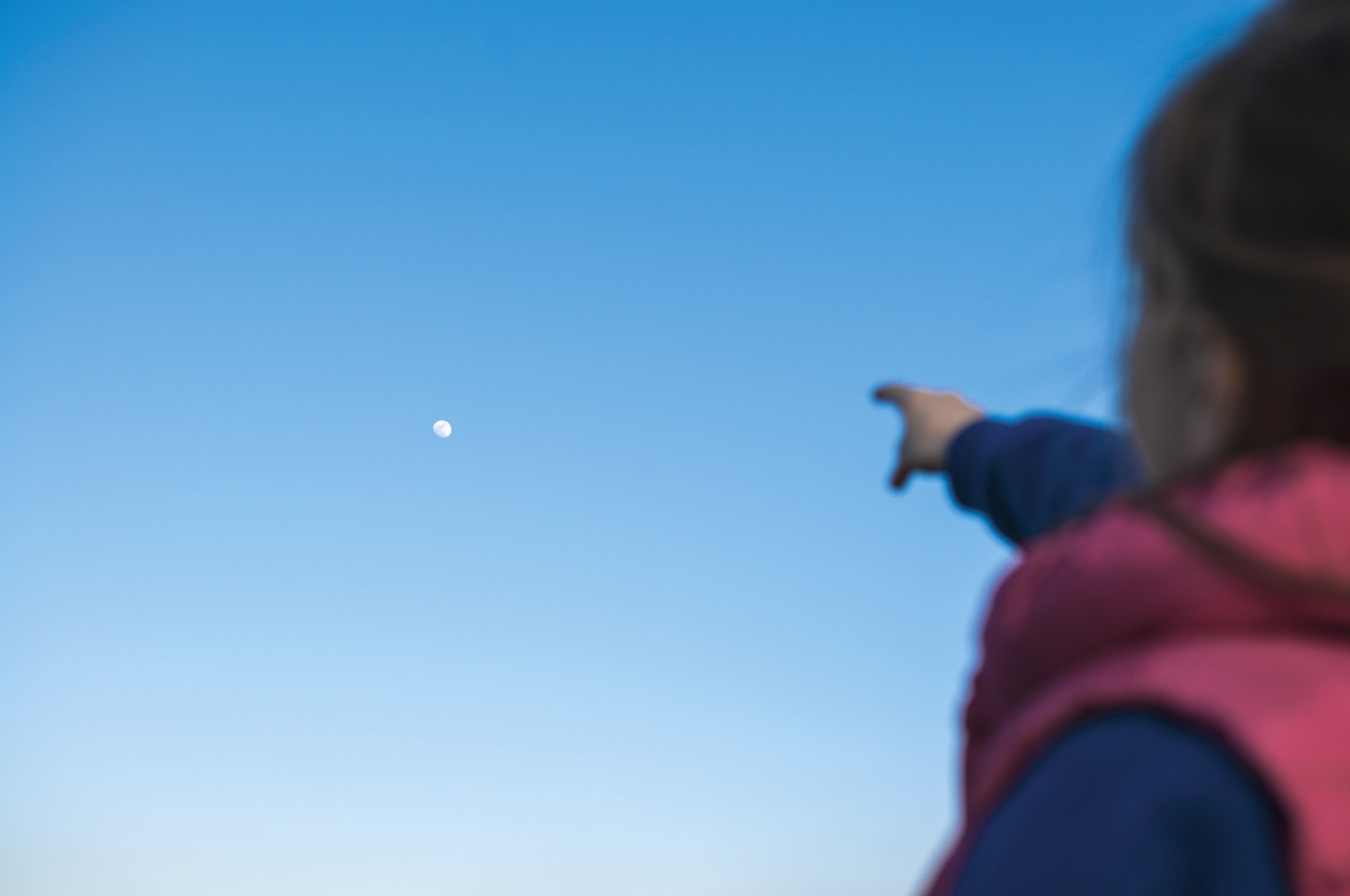 Ein Kind zeigt mit ausgestrecktem Zeigefinger auf den Mond am Abendhimmel.