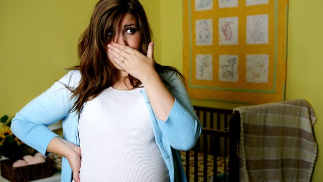 Eine schwangere Frau hält sich die Hand vor den Mund. Sie leidet offenbar unter Übelkeit.