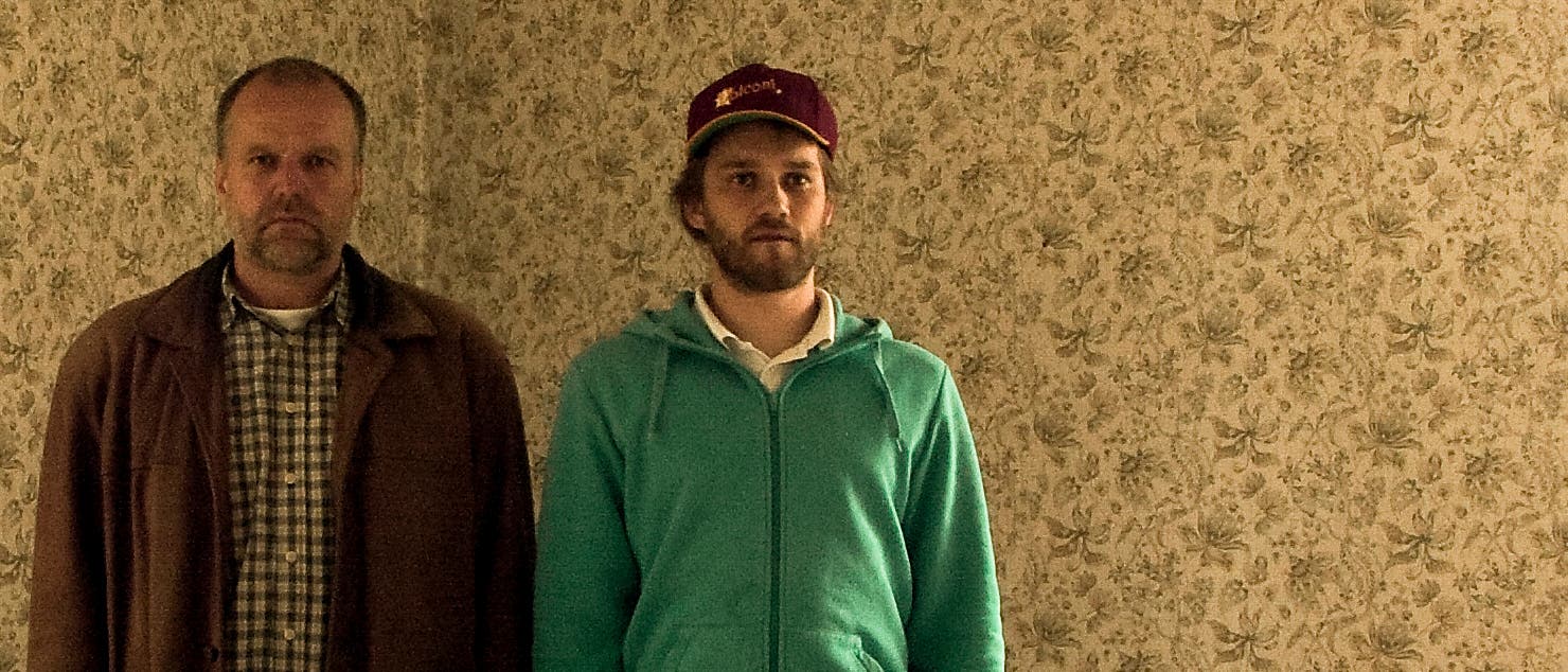 Vater und Sohn stehen in einem leeren Wohnraum, der von einer auffälligen alten Tapete geziert wird. Vater und Sohn stehen in einem leeren Wohnraum, der von einer auffälligen alten Tapete geziert wird.