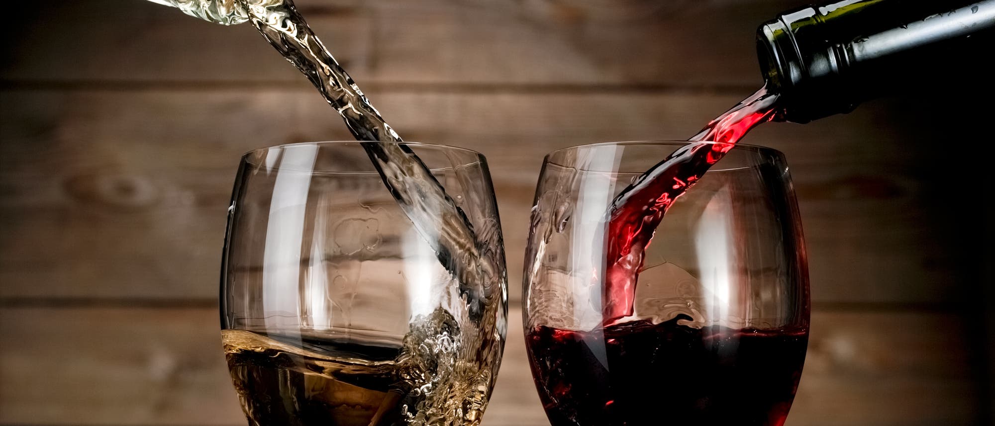 Rotwein und Weißwein werden aus der Flasche ins Glas eingeschenkt. Rotwein und Weißwein werden aus der Flasche ins Glas eingeschenkt.
