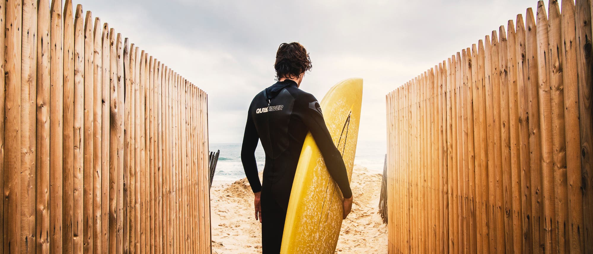 Ein Surfer mit seinem Board am Strand zwischen Palisaden. Ein Surfer mit seinem Board am Strand zwischen Palisaden.