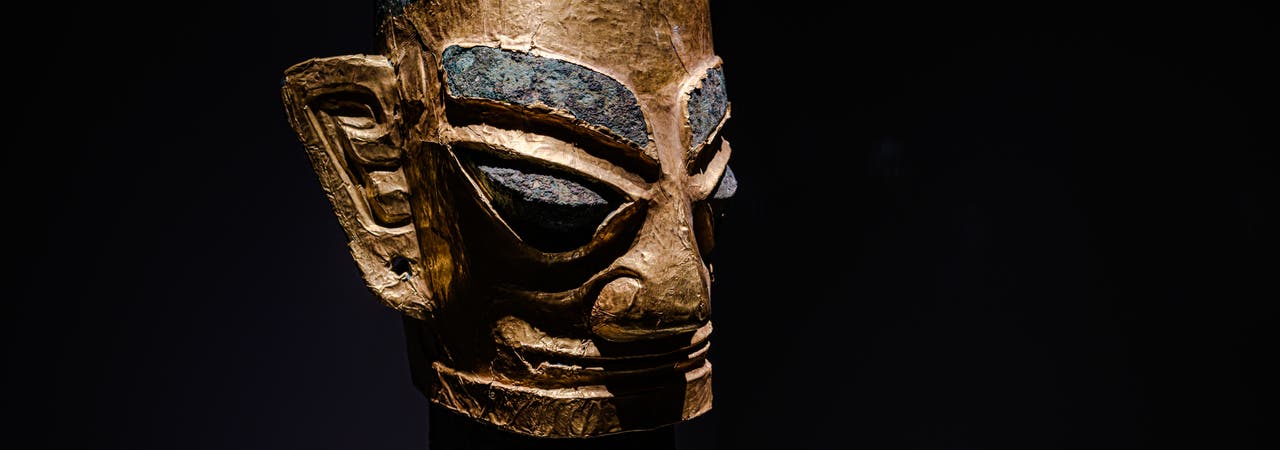 Spitze Augen, große Ohren, kantige Gesichtszüge – der Kopf aus Bronze zeigt die für die Sanxingdui-Kultur typischen Stilformen. Das Gesicht ist mit einer dünnen Goldfolie belegt. Die Skulptur kam in einer von acht großen Opfergruben ans Licht.