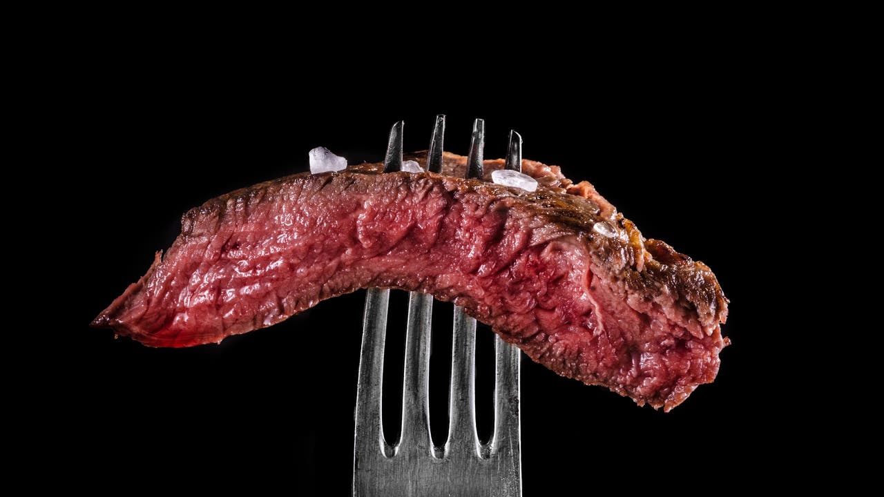 Ein Stück medium rare Steak auf einer Gabel vor schwarzem Hintergrund