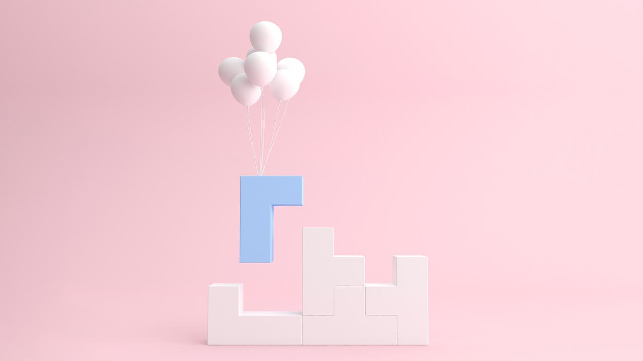 Ein hellblauer, L-förmiger Baustein schwebt über einer Struktur aus weißen, ineinandergreifenden Blöcken. Der blaue Block wird von mehreren weißen Luftballons getragen. Der Hintergrund ist ein sanftes Rosa, das eine ruhige und minimalistische Atmosphäre schafft.