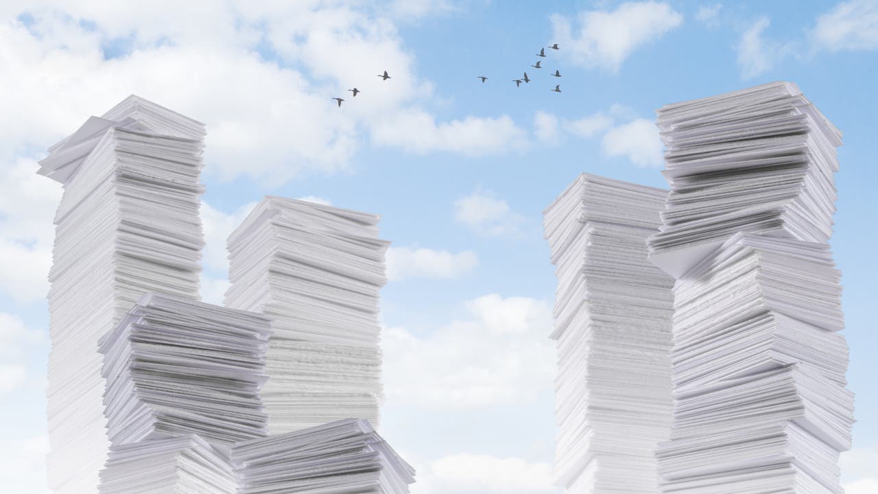 Hohe Stapel von weißen Papierblättern ragen in den Himmel, der mit weißen Wolken und fliegenden Vögeln bedeckt ist. Die Szene vermittelt ein Gefühl von Überfluss und Büroarbeit. Es gibt keine Menschen oder Text im Bild.