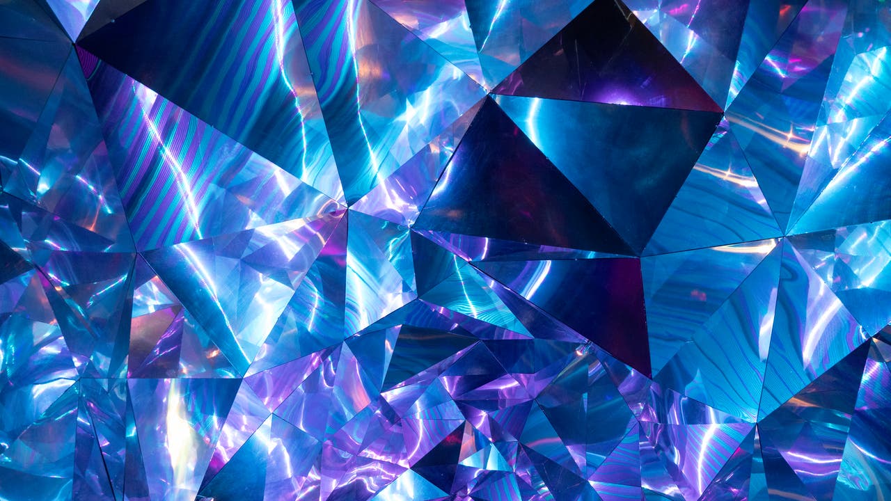 Ein abstraktes Kunstwerk mit einer Vielzahl von facettierten, prismatischen Formen in schimmernden Blau- und Violetttönen. Die geometrischen Muster reflektieren Licht und erzeugen einen kaleidoskopischen Effekt, der an Edelsteine oder Kristalle erinnert. Die Komposition vermittelt ein Gefühl von Tiefe und Bewegung.