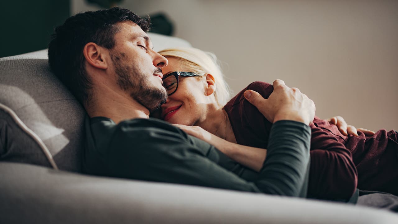 Mann und Frau auf dem Sofa, sie kuschelt, er schläft