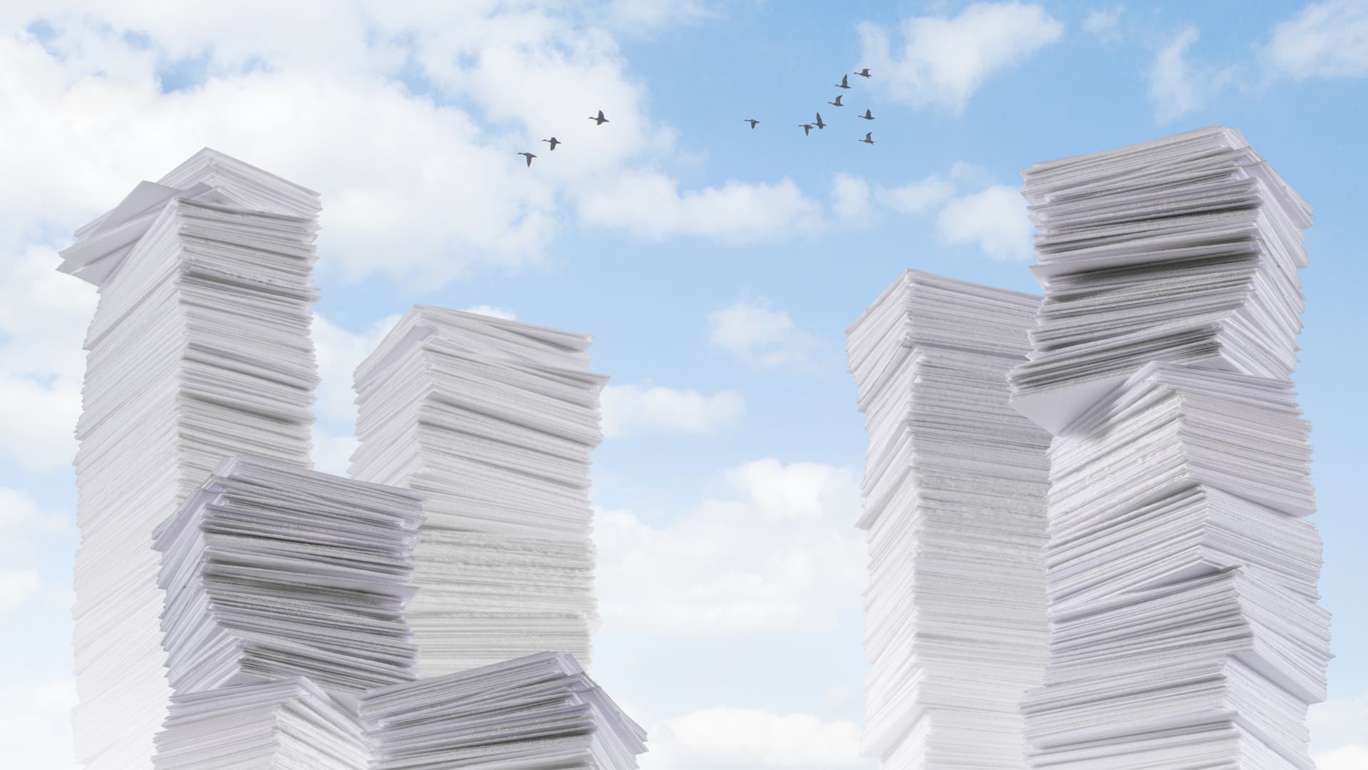 Hohe Stapel von weißen Papierblättern ragen in den Himmel, der mit weißen Wolken und fliegenden Vögeln bedeckt ist. Die Szene vermittelt ein Gefühl von Überfluss und Büroarbeit. Es gibt keine Menschen oder Text im Bild.