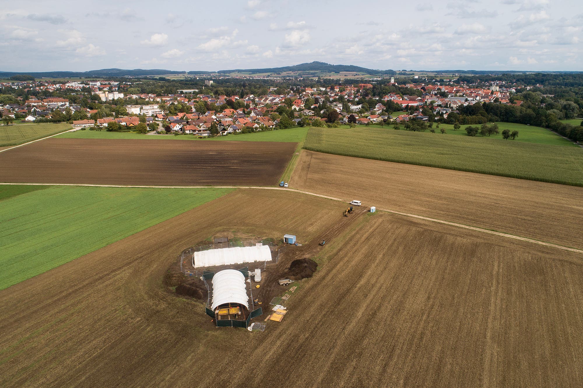 Drohnenaufnahme mit der Grabungsstätte im Vordergrund, Riedlingen im Mittelgrund und dem Bussen im Hintergrund.