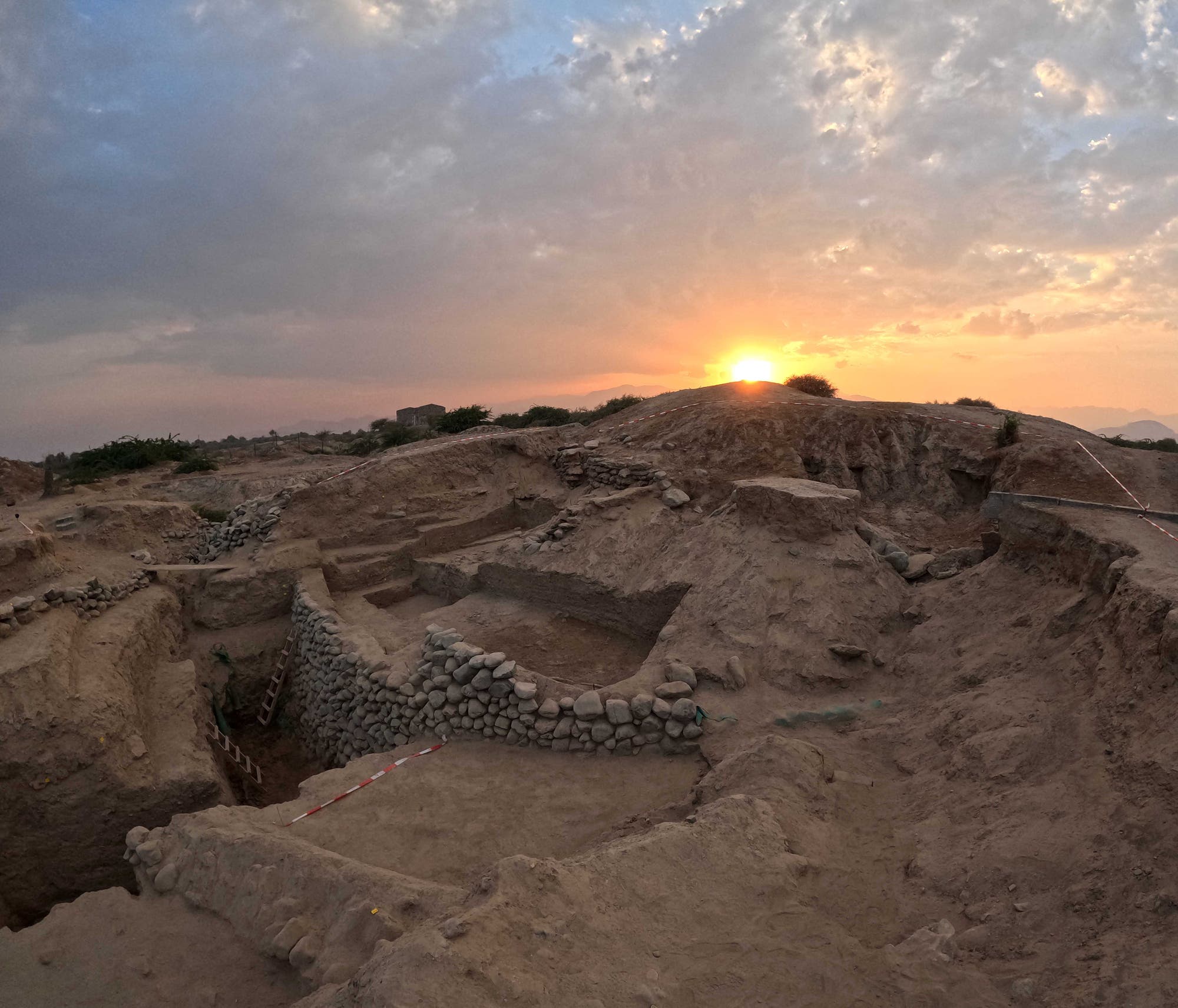 Ein Erdhügel mit frei gelegten Steinmauern: Die Ausgrabungsstätte Kalba in den Vereinigten Arabischen Emiraten während der Abenddämmerung.