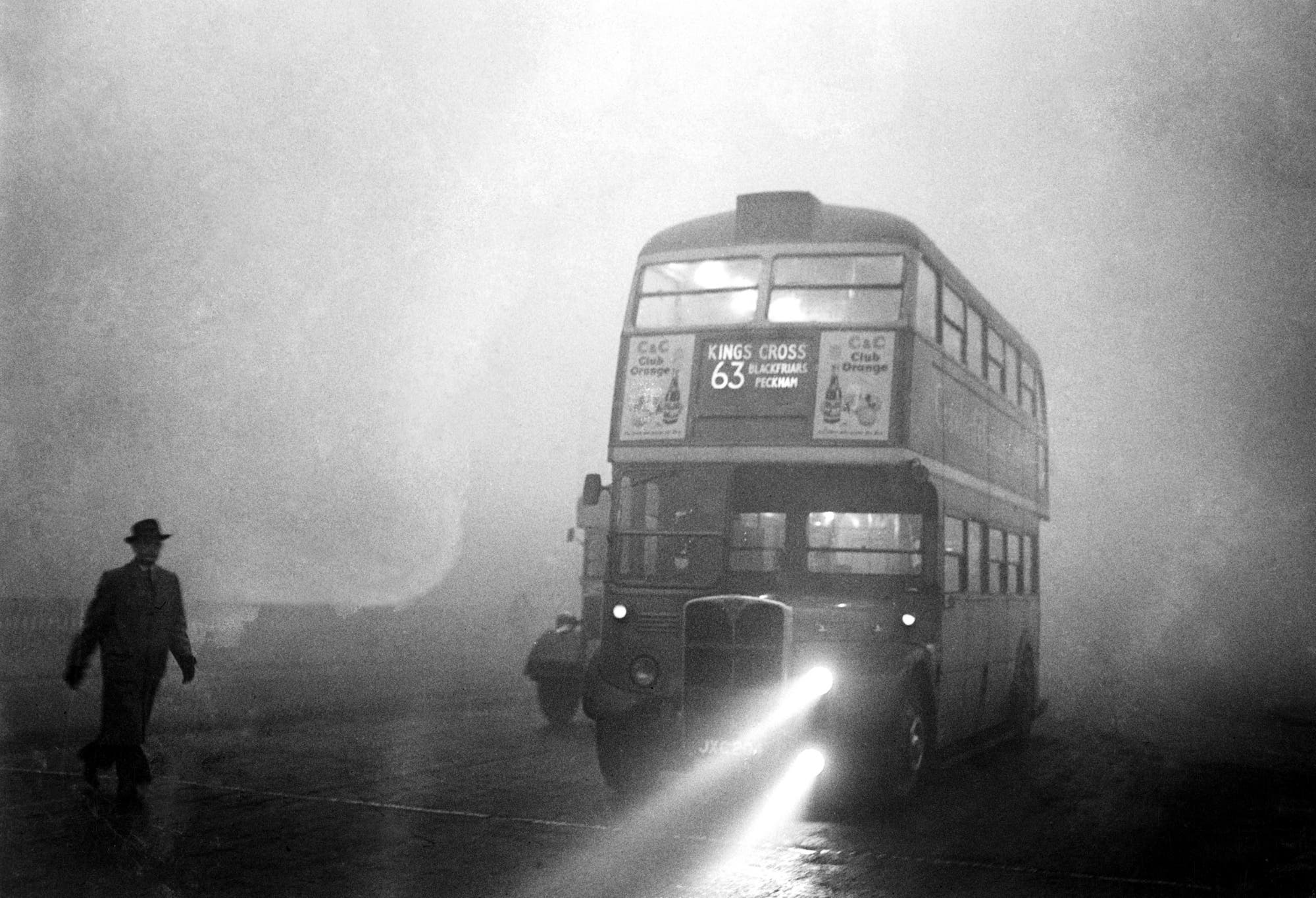 Ein Bus ebnet sich, ausgerüstet mit starken Scheinwerfern, den Weg durch den dichten Smog von London im Jahr 1952.