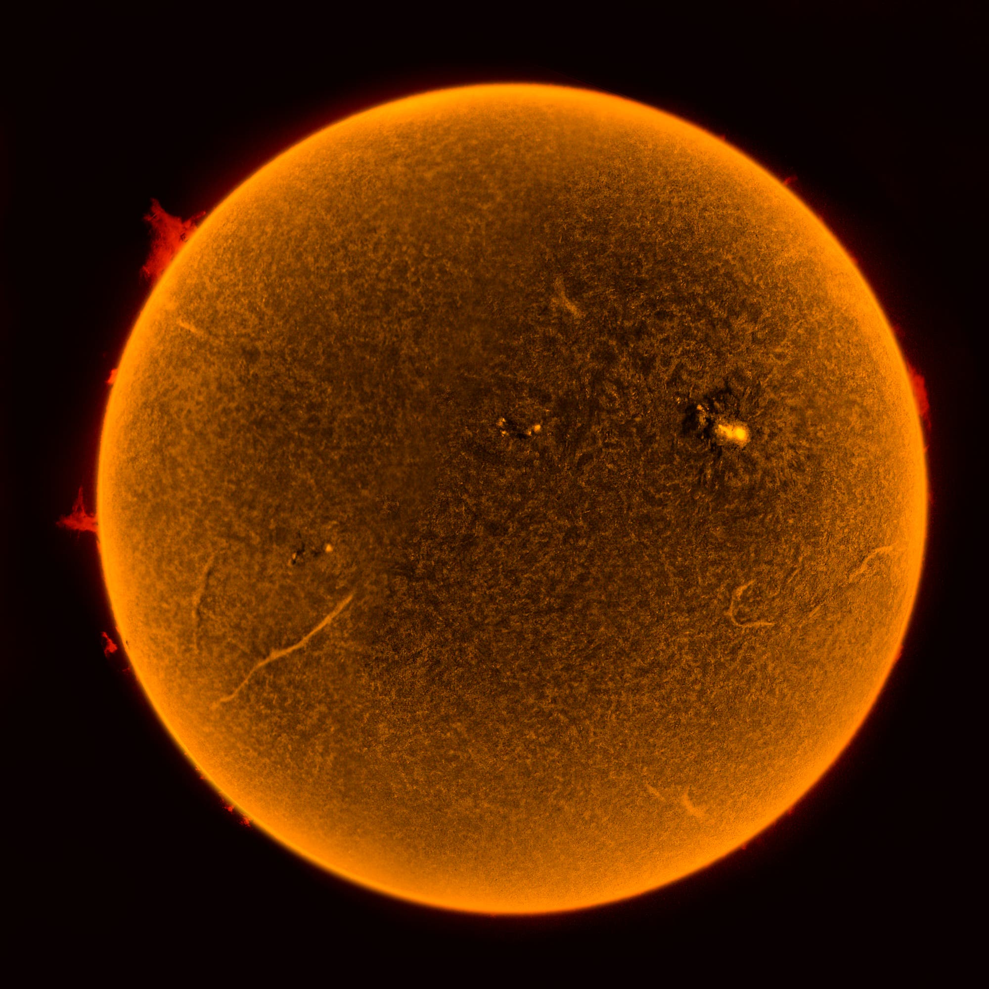 Eine detaillierte Aufnahme der Sonne, die ihre Oberfläche in leuchtendem Orange zeigt. Sichtbar sind Sonnenflecken und Protuberanzen, die als helle und dunkle Bereiche erscheinen. Die Textur der Sonnenoberfläche ist deutlich erkennbar, was die dynamische Aktivität der Sonne verdeutlicht. Der Hintergrund ist dunkel, was den Kontrast zur leuchtenden Sonne verstärkt. Schlüsselwörter: Sonne, Sonnenflecken, Protuberanzen, Astronomie, Sonnenoberfläche.