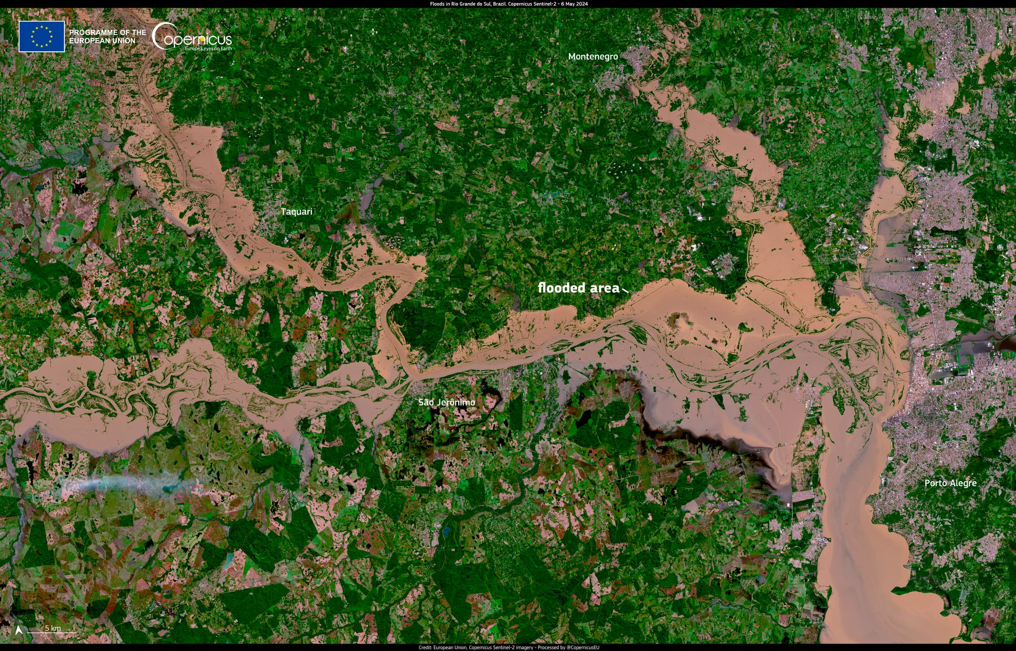 Satellietfoto van Rio Grande do Sul: Delen van de regio zijn ondergedompeld in bruine waterlichamen - inclusief de stad Porto Alegre, die kan worden gezien als een grijs gebied aan de rechterkant van het beeld.  De niet-overstroomde gebieden bestaan ​​uit boseilanden en landbouwgebieden met verschillende tinten groen