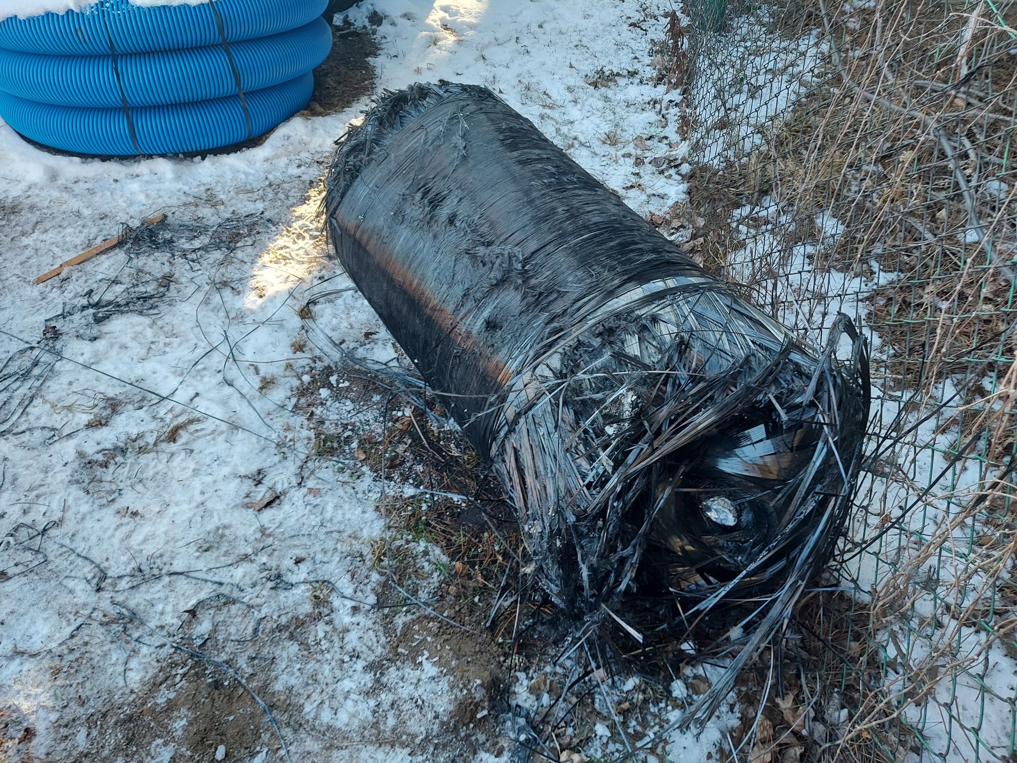 Ein großer, beschädigter Zylinder aus schwarzem Material liegt auf schneebedecktem Boden.