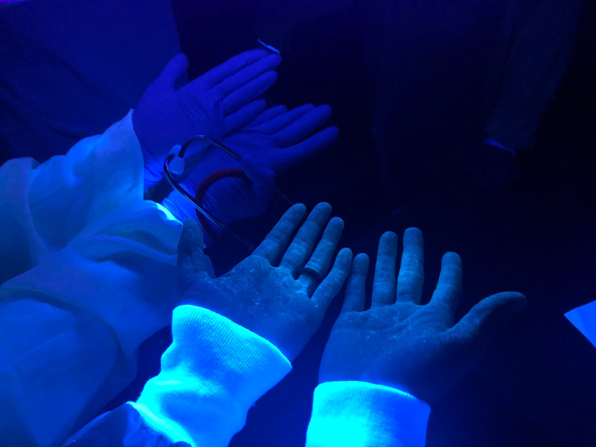 Hände mit Spritzern einer Fluoreszenzfarbe unter UV-Licht.