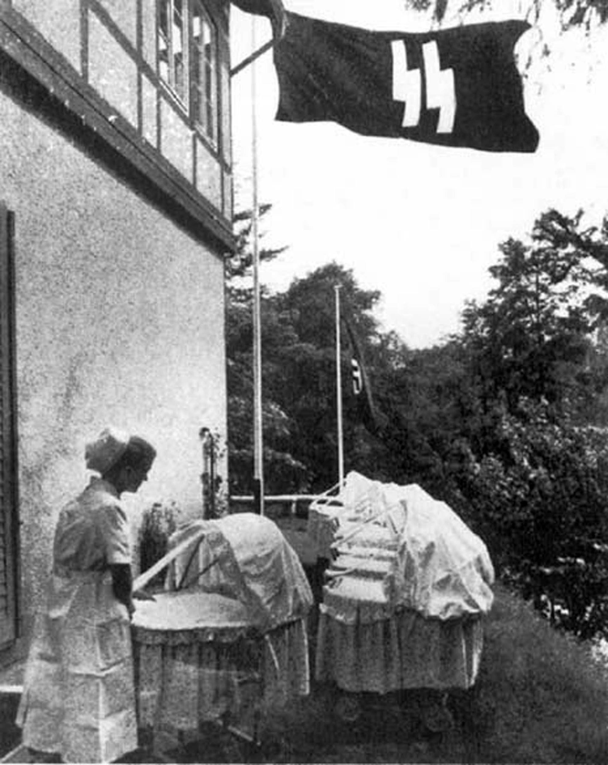 In dem Bild aus dem Jahr 1943 schiebt eine Krankenschwester Kinderwagen vor einem Lebensborn-Heim, darüber die Fahne der SS. 