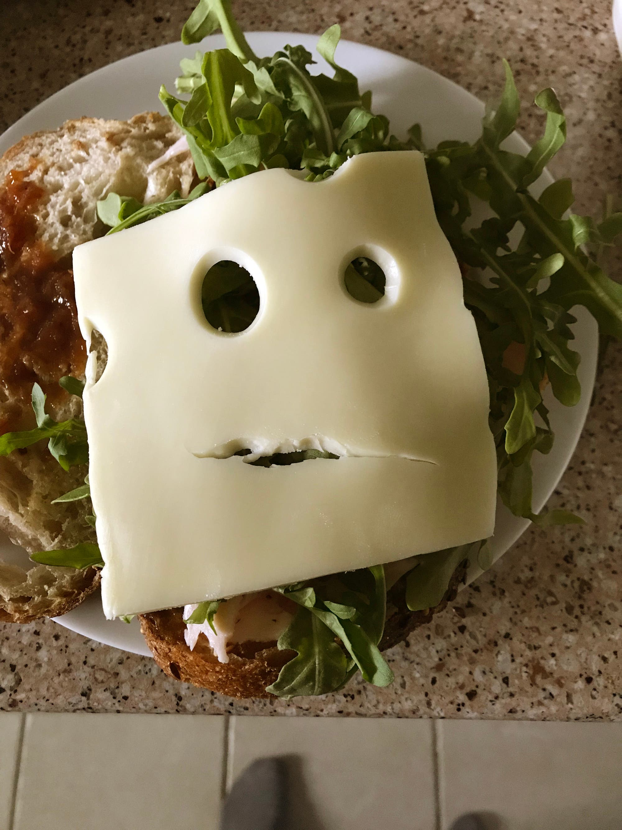 Belegtes Brot mit Rucola und einer Scheibe Käse, das wie ein Gesicht aussieht