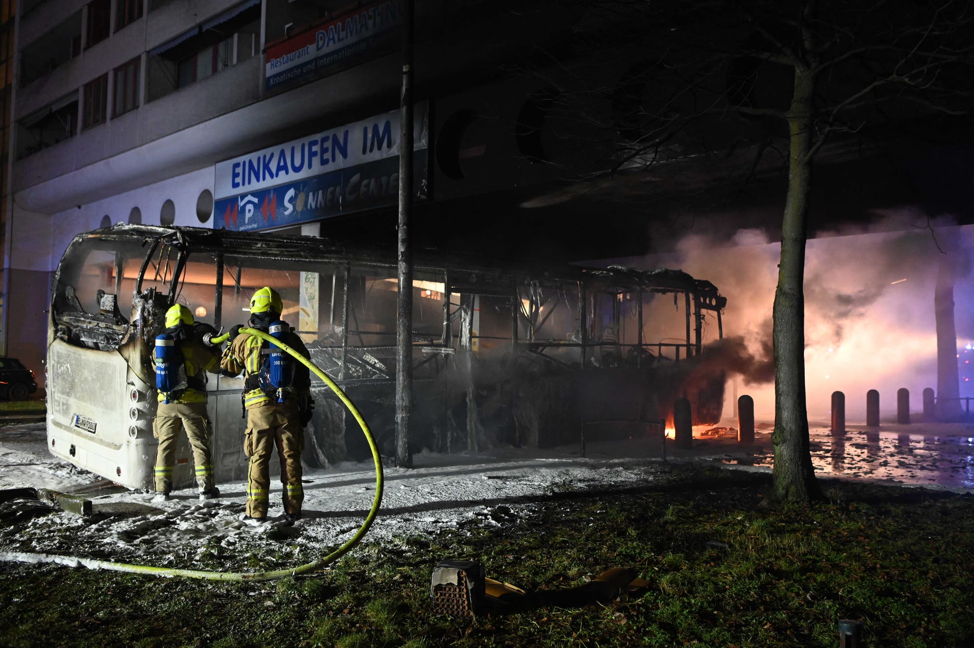 Einsatzkräfte der Feuerwehr löschen in der Silvesternacht 2022/23 an der Sonnenallee im Bezirk Neukölln einen brennenden Bus