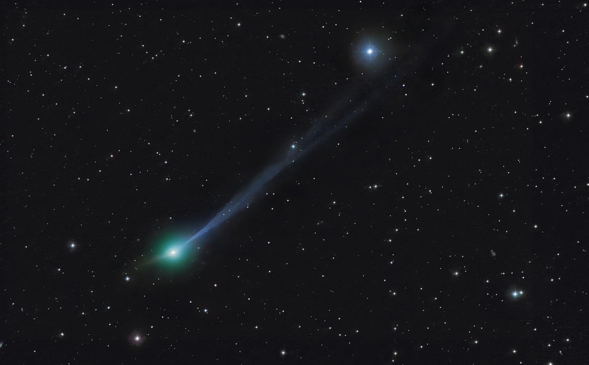 Ein Komet mit einem leuchtend gr&uuml;nen Kopf und einem langen, bl&auml;ulichen Schweif zieht durch ein Sternenfeld. Der Hintergrund ist mit zahlreichen kleinen, funkelnden Sternen &uuml;bers&auml;t. Der Komet scheint sich von links unten nach rechts oben zu bewegen. Die Szene vermittelt ein Gef&uuml;hl von Bewegung und Weite im Weltraum.