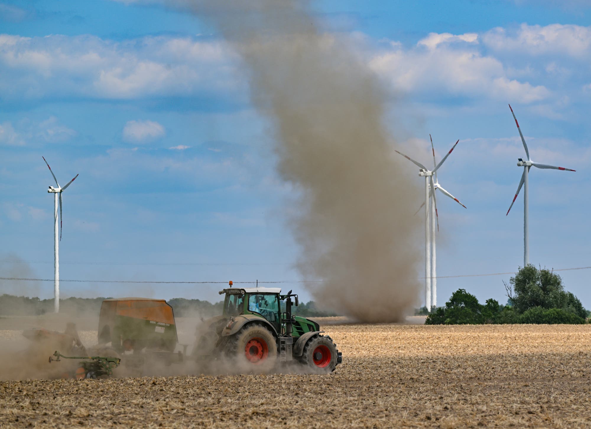 Hinter einem Traktor, der eine Staubschleppe hinter sich herzieht, erkennt man eine Windhose aus aufgewirbeltem Staub