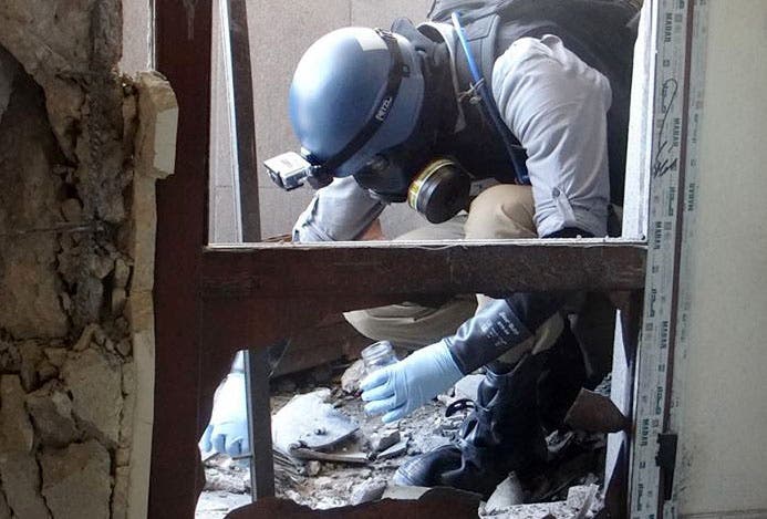 Ein Mann mit blauem Helm und Gasmaske füllt in einer Ruine Schutt vom Boden in ein Probenglas.
