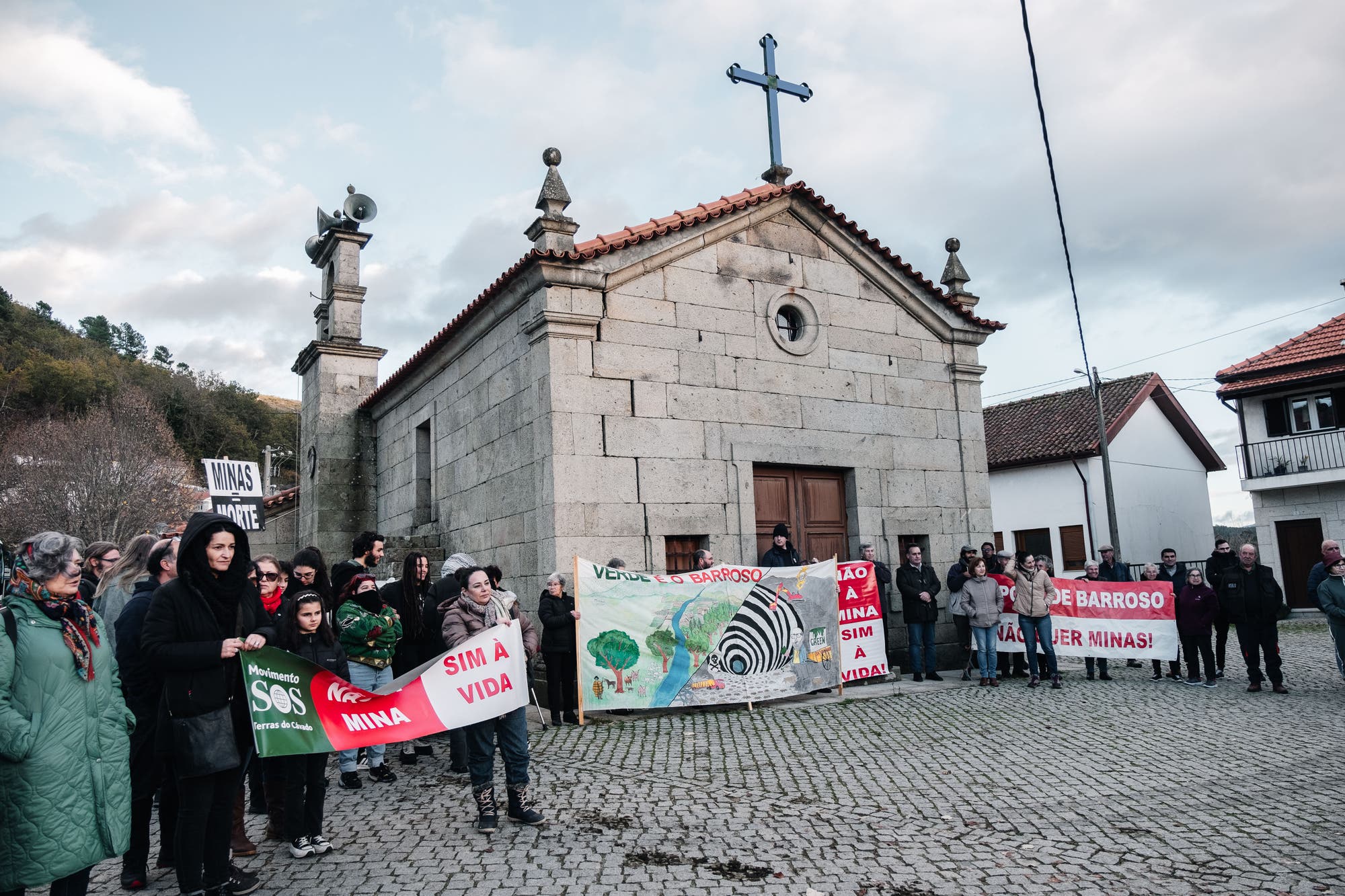 eine kleine Steinkirche auf einem gepflasterten Platz, davor Protestierende mit Plakaten