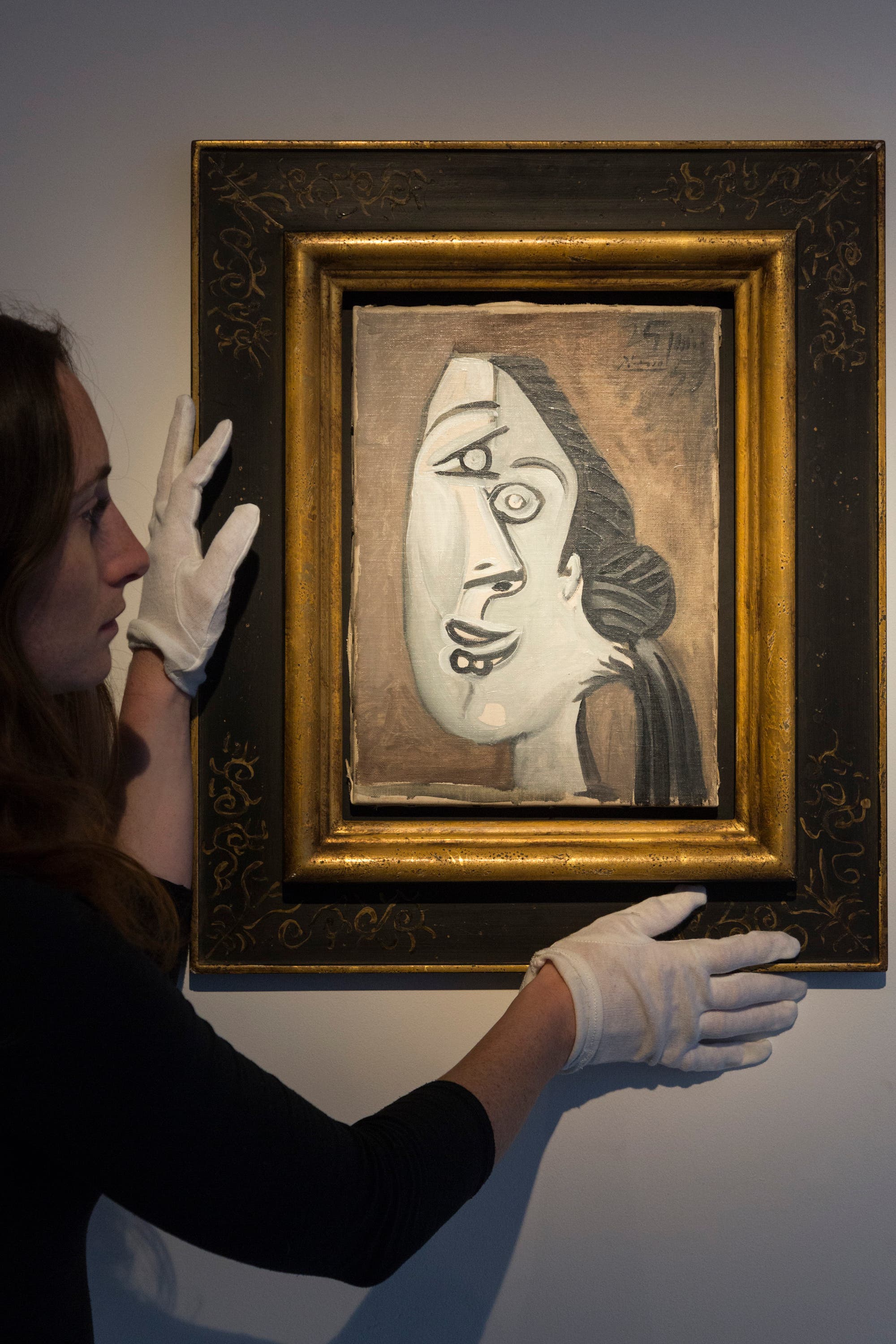 Junge Frau hängt ein Gemälde von Pablo Picasso auf: einen Frauenkopf mit vertikal verschobenen Gesichtshälften