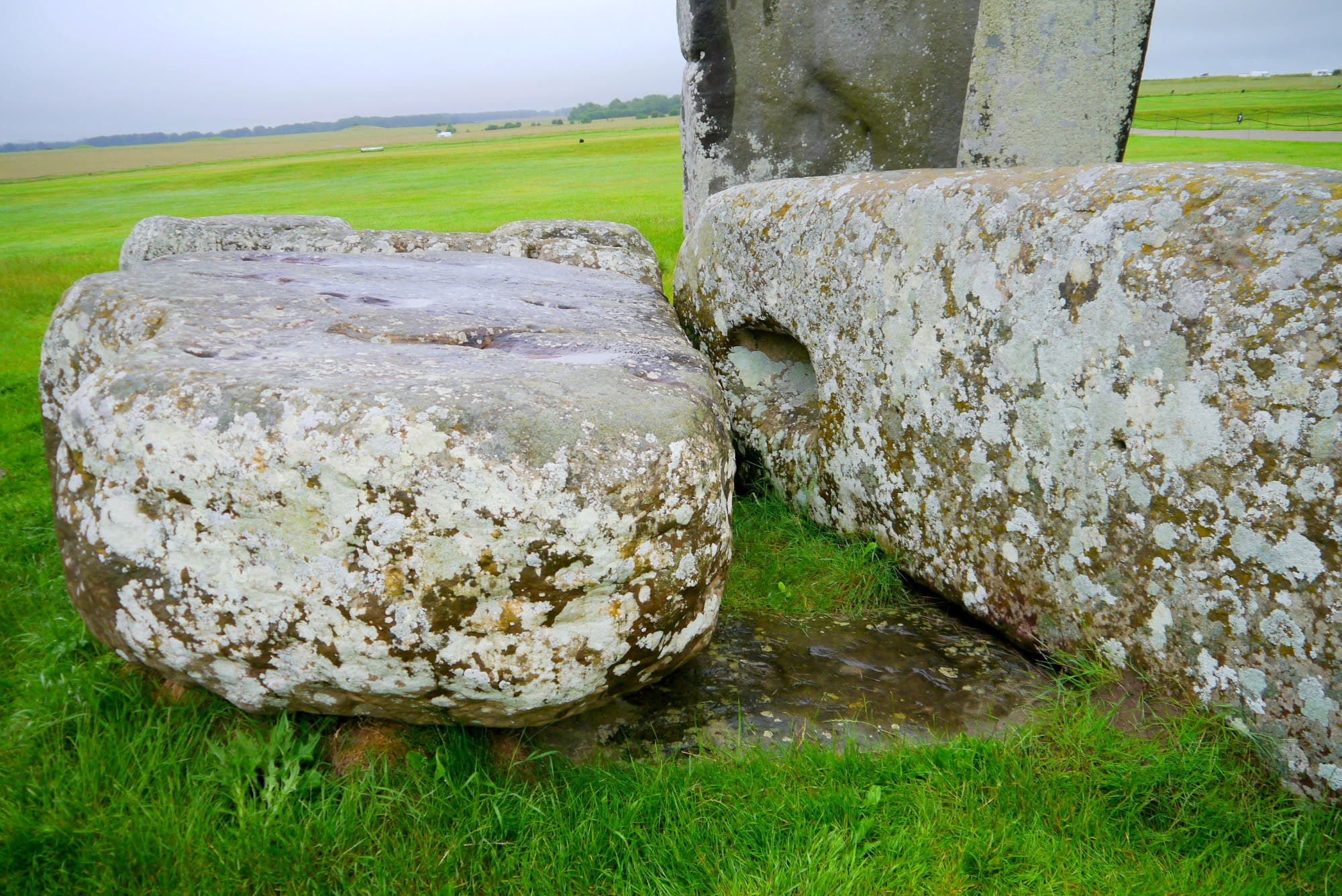 Blick auf den Altar Stone in Stonehenge, der nahezu vollständig in der Erde liegt und von zwei herabgestürzten Monolithen bedeckt wird.