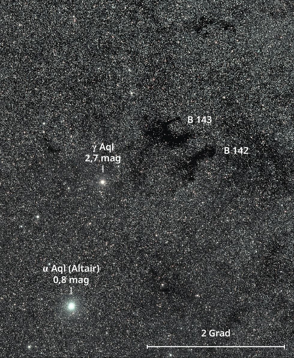 Die benachbarten Dunkelwolken B 142/143 verdecken dahinterliegende Sterne. Die Form des verdunkelten Bereichs erinnert an den Buchstaben E.