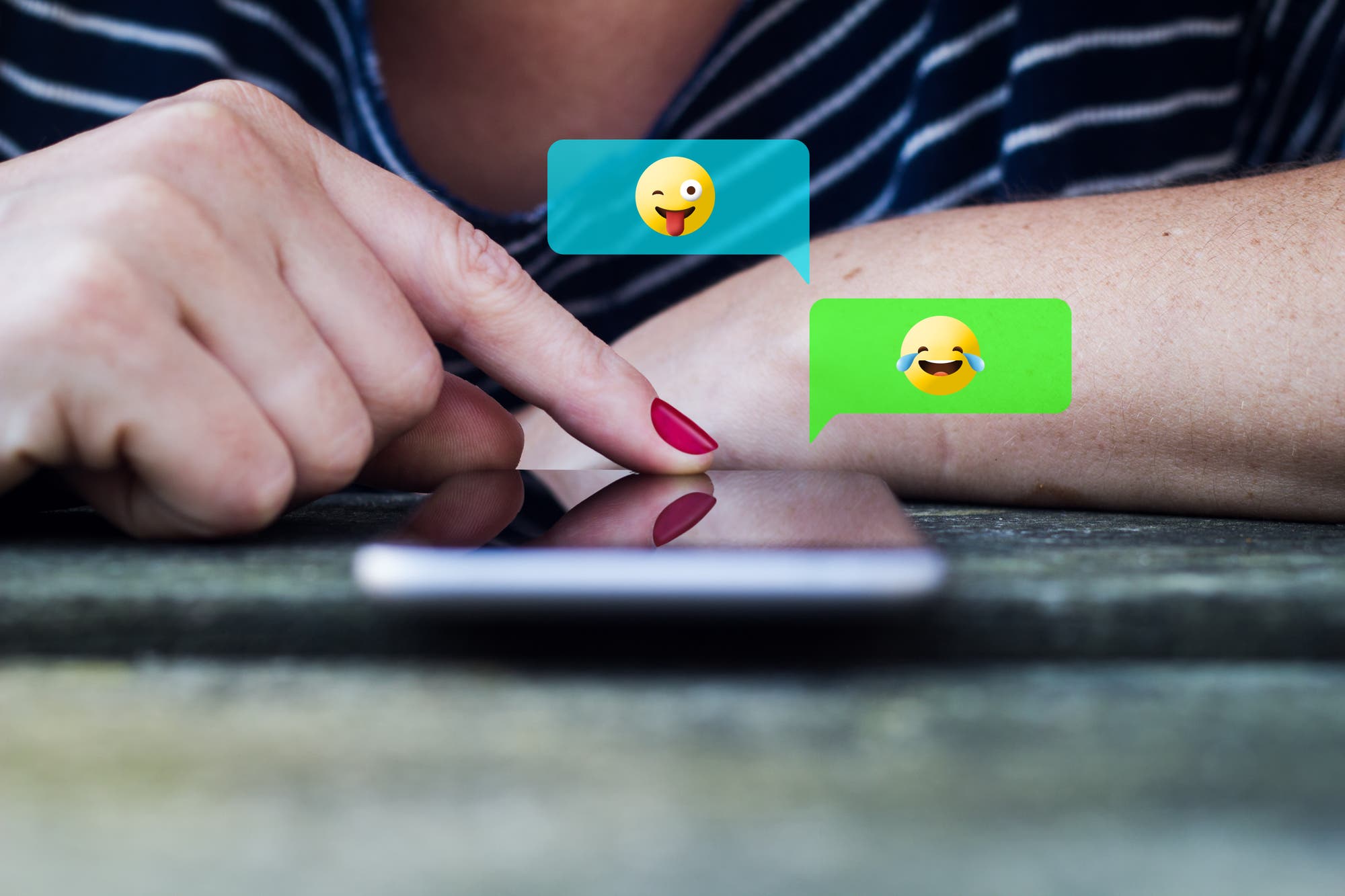 Eine Frau benutzt Emojis in einer Konversation mit Smartphone. Nicht so wie früher, als man noch mühevoll ASCII-Smileys basteln musste. Wir hatten ja nix, damals. 