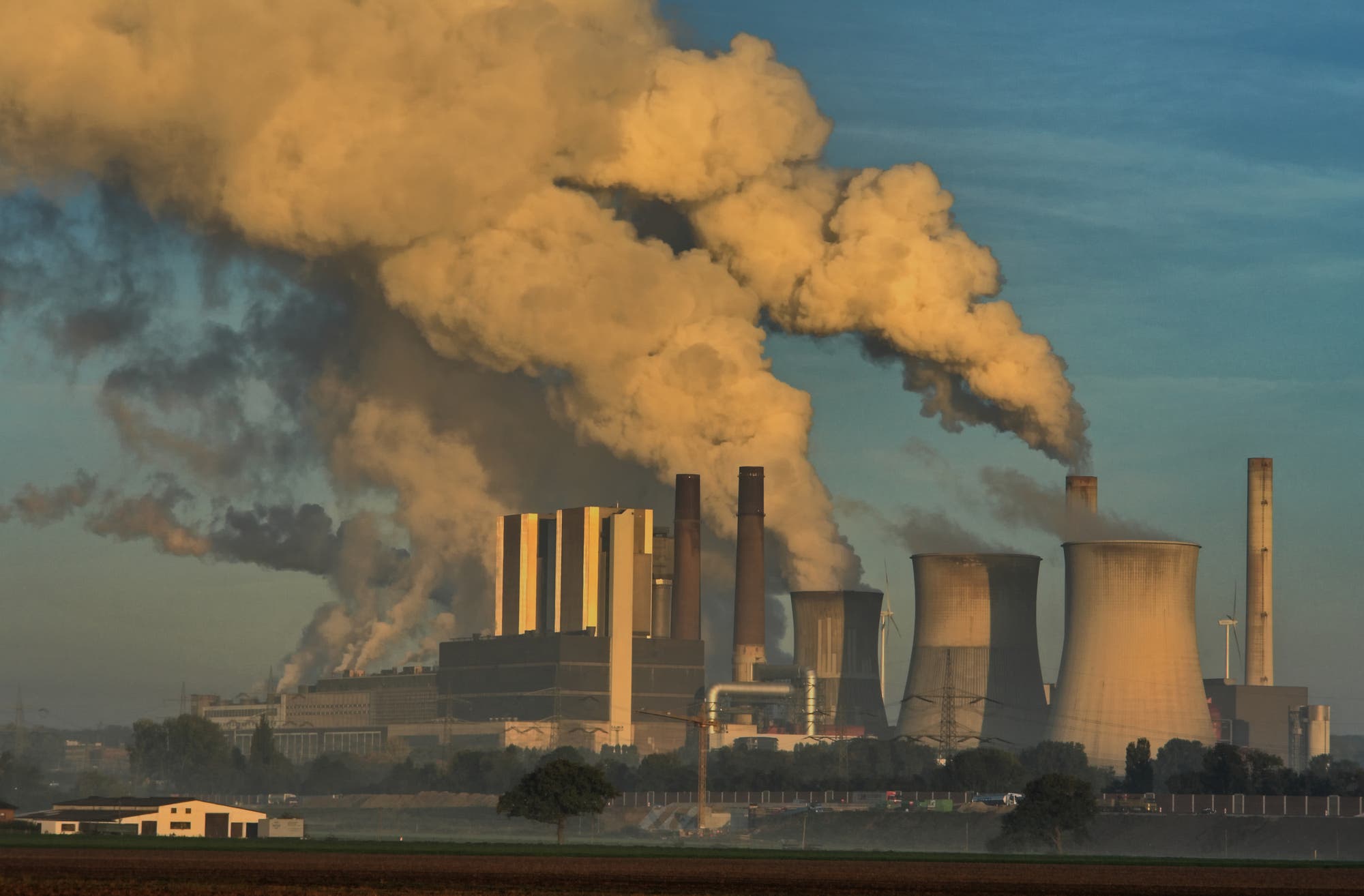 Ein Kohlekraftwerk mit rauchenden Schornsteinen vor blauem Himmel.