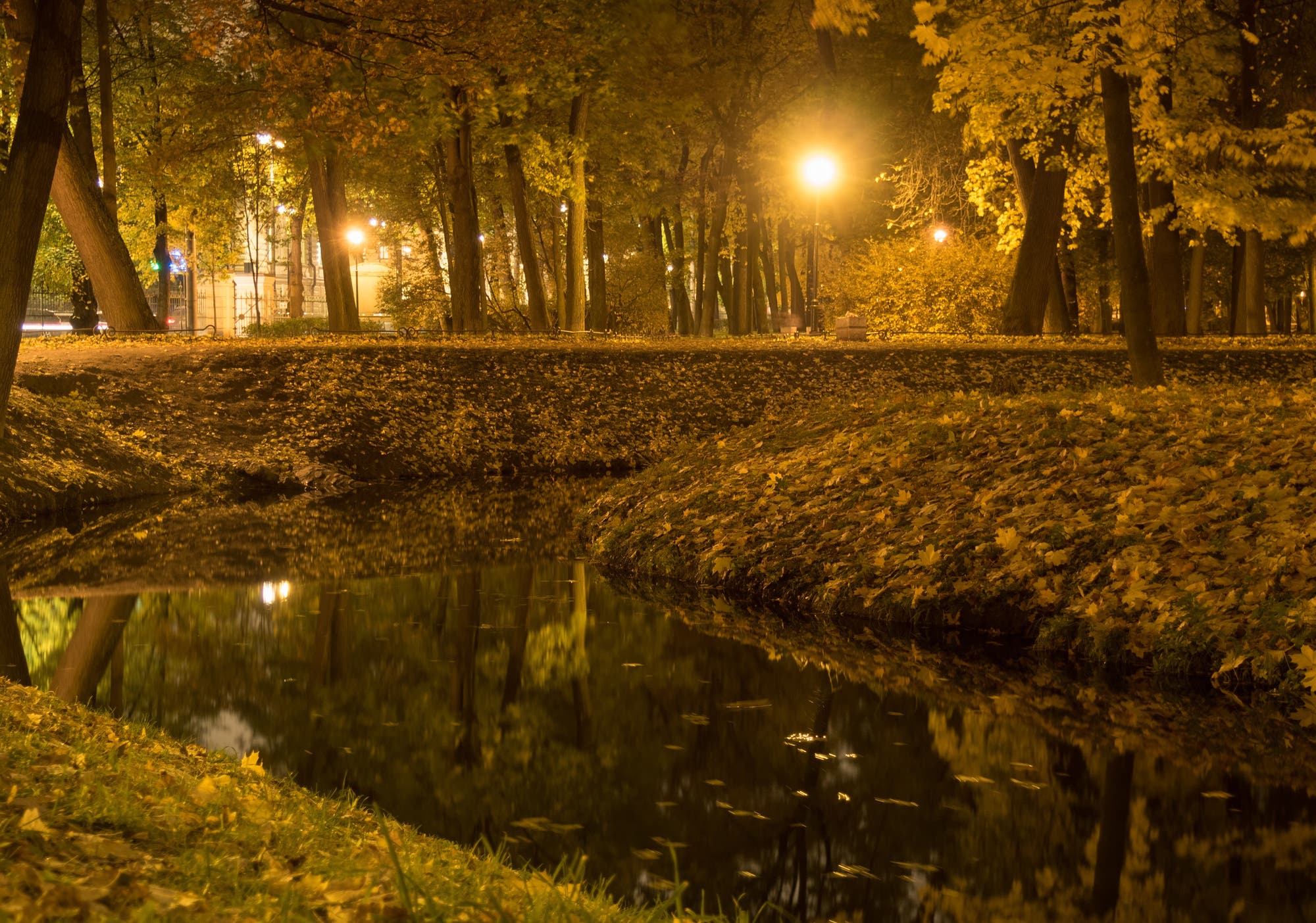 Ein Stadpark mit einem kanalisierten Bach im Vordergrund und künstlicher Beleuchtung im Hintergrund.
