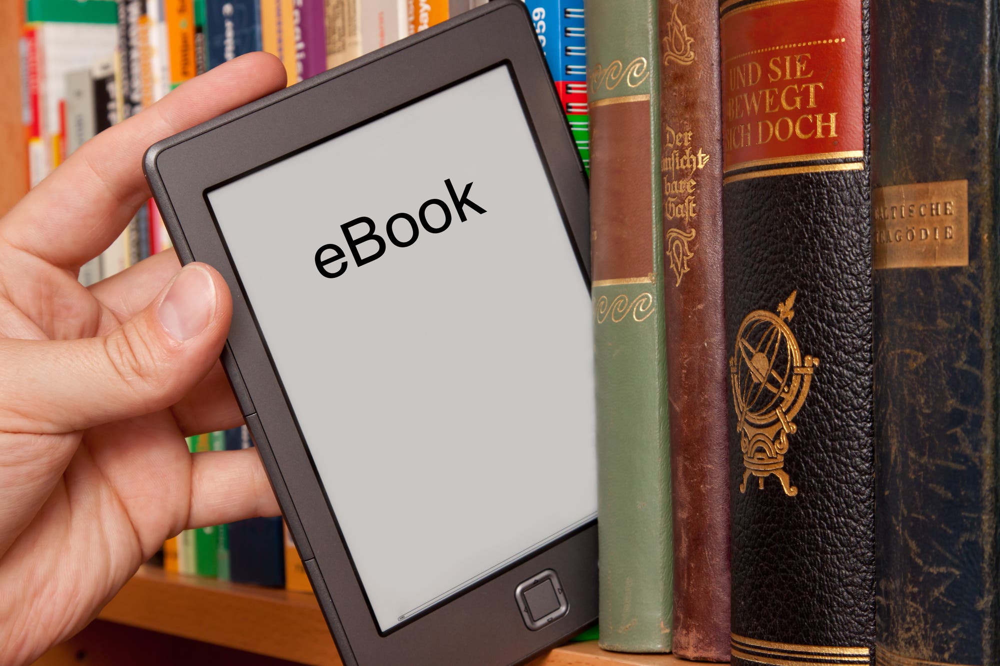 Eine Hand nimmt ein E-Book zwischen Büchern aus dem Bücherregal.