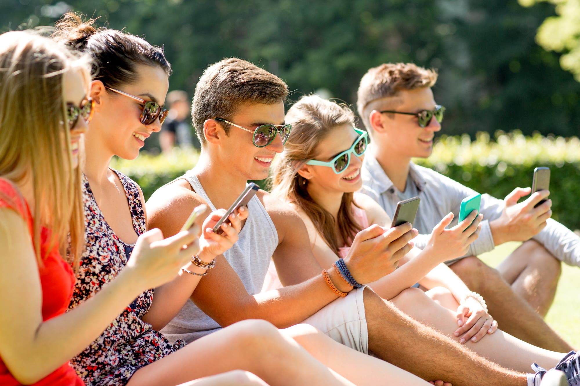 Junge Menschen sitzen mit Smartphone in der Sonne