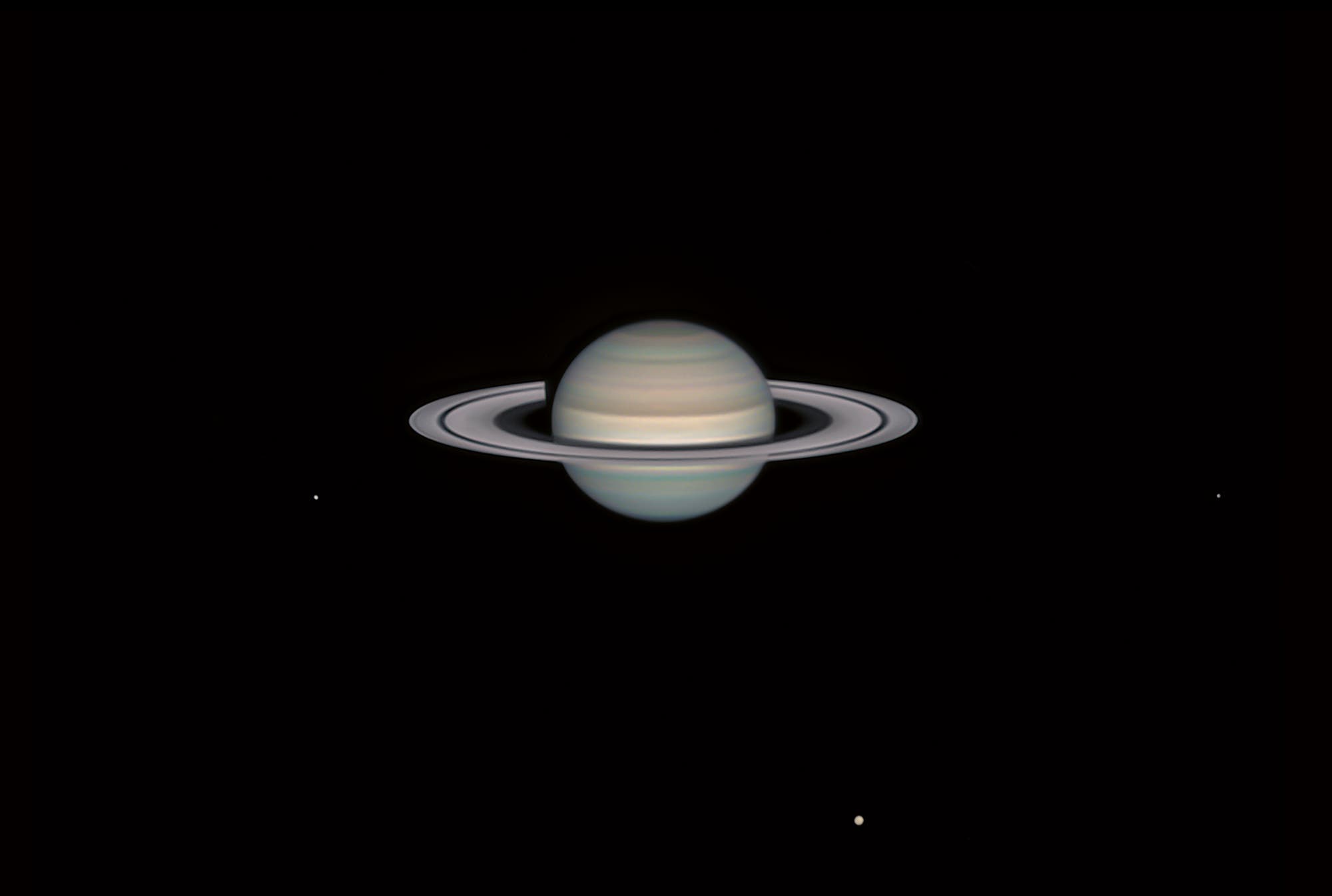 Saturn mit seinem Ringsystem sowie den Monden Tethys, Titan und Dione