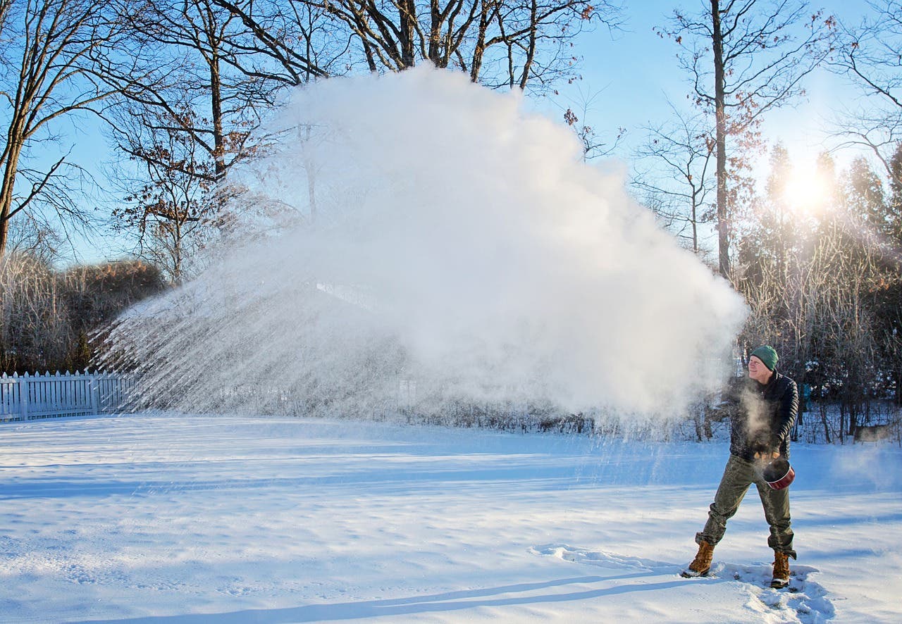 Bild eines Mannes, der kochendes Wasser in eine schneebedeckte Landschaft schleudert