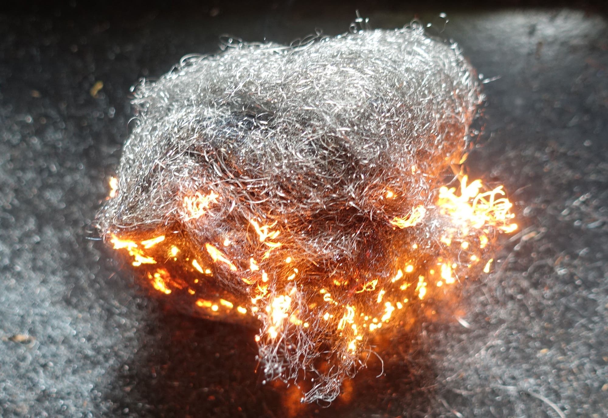 In einem brennenden Bündel Stahlwolle, das auf einer Platte liegt, glühen zahlreiche der Metallfasern orange-gelb.